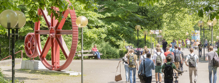 Students in summer on north campus, red gears in background