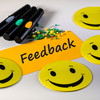 Foto: Moderationskarte mit dem Schriftzug "Feedback", gelbe Smilies, Stifte und Moderationsnadeln