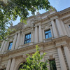 A sandstone-colored old building with large windows from the frog's perspective.