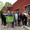 Eine Gruppe von Menschen steht vor dem Internationalen Begegnungszentrum (IBZ). Drei Menschen im Vordergrund halten eine Fahne mit dem Logo der TU Dortmund. 