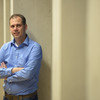 Portrait photo of Daniel Neider leaning against a concrete wall in a blue shirt, arms crossed and smiling slightly.