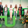 Three young female students stand between a man and a woman. All three are holding certificates in their hands, with a large TU logo on the floor in the foreground.