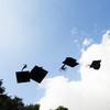 Four black doctor hats flying in the air in front of blue sky with white clouds.