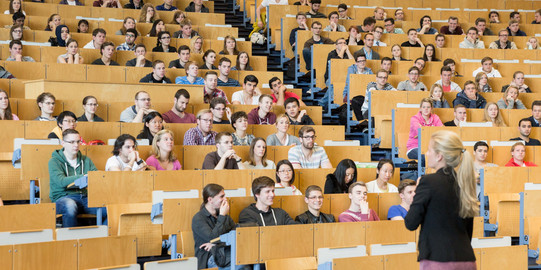 A lecturer stands in front of students in the lecture hall. 