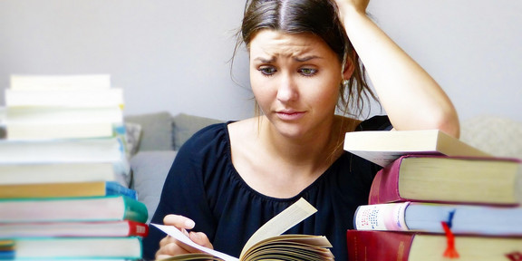 A woman looks strained at a book while resting her head on her arm.